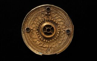 Scheibenfibel, 7. Jh. | Mit Perldraht verzierte Scheibenfibel mit Mittelbuckel. In dem von einer Buckelreihe umsäumten Mittebuckel waren ursprünglich wohl Almandine eingesetzt, wie auch in die vier kleinen, kreuzförmig am äußeren Rand angeordneten Buckel. Die Schauseite aus Gold ist außerdem mit Filigrandrahtauflagen geschmückt. | Fundort: Gammertingen | Herkunft/Rechte: Landesmuseum Württemberg, Hendrik Zwietasch (CC BY-SA 4.0)