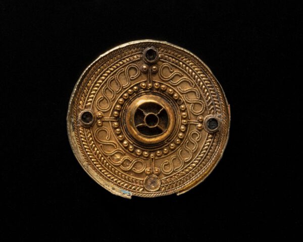 Scheibenfibel, 7. Jh. | Mit Perldraht verzierte Scheibenfibel mit Mittelbuckel. In dem von einer Buckelreihe umsäumten Mittebuckel waren ursprünglich wohl Almandine eingesetzt, wie auch in die vier kleinen, kreuzförmig am äußeren Rand angeordneten Buckel. Die Schauseite aus Gold ist außerdem mit Filigrandrahtauflagen geschmückt. | Fundort: Gammertingen | Herkunft/Rechte: Landesmuseum Württemberg, Hendrik Zwietasch (CC BY-SA 4.0)